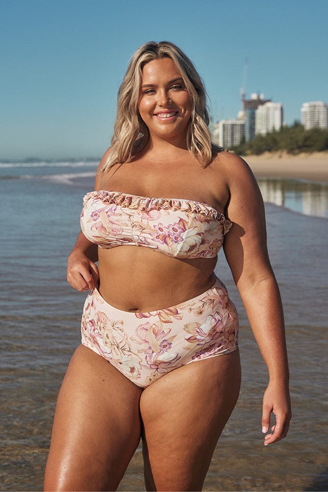 Blonde model wearing blush pink floral high waisted swim pant on beach