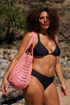 model holding peach beach bag wearing black bikini