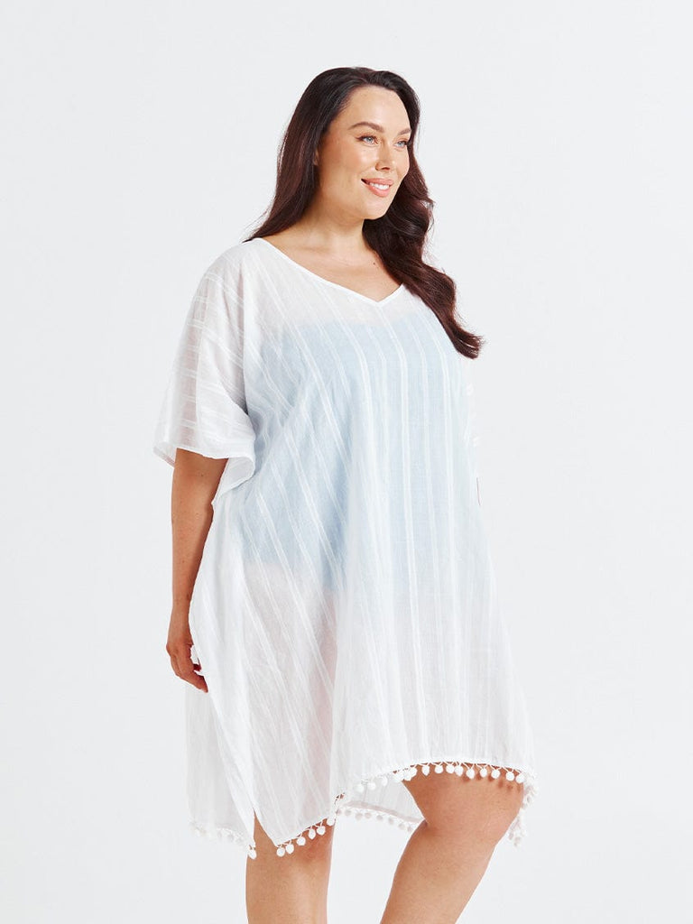Woman wearing a white cover-up with pom-pom trim on a plain background