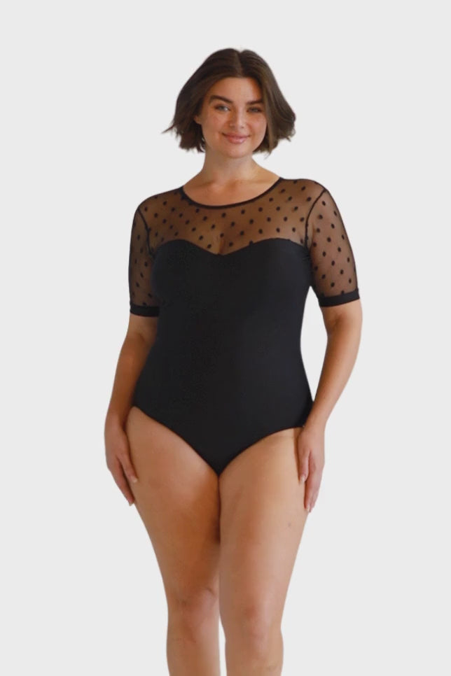 Brunette model wears mesh polkadot black modest one piece swimsuit