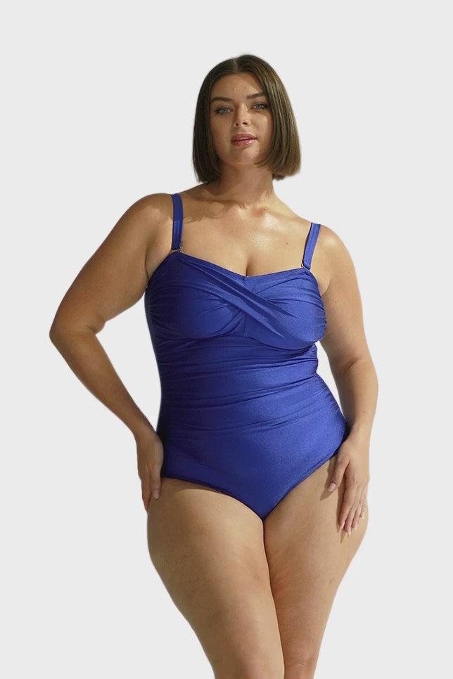 Brunette model wears sapphire blue bandeau one piece swimsuit with tummy ruching and removable straps