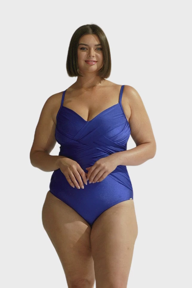 brunette women wears criss cross one piece swimsuit in metallic royal blue