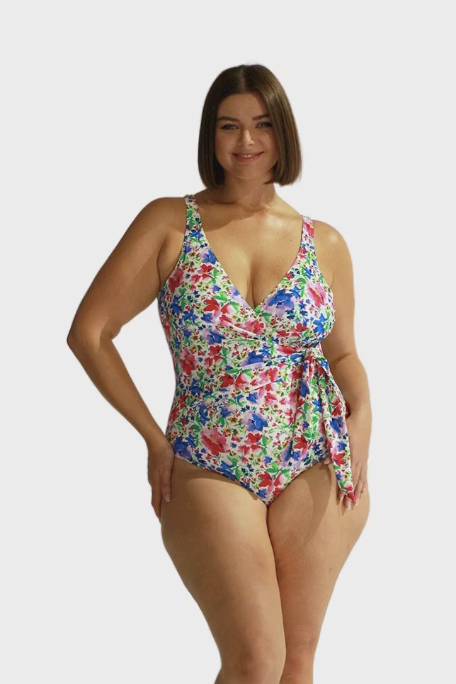 brunette model wears wrap one piece with low v neck in pink and blue floral print