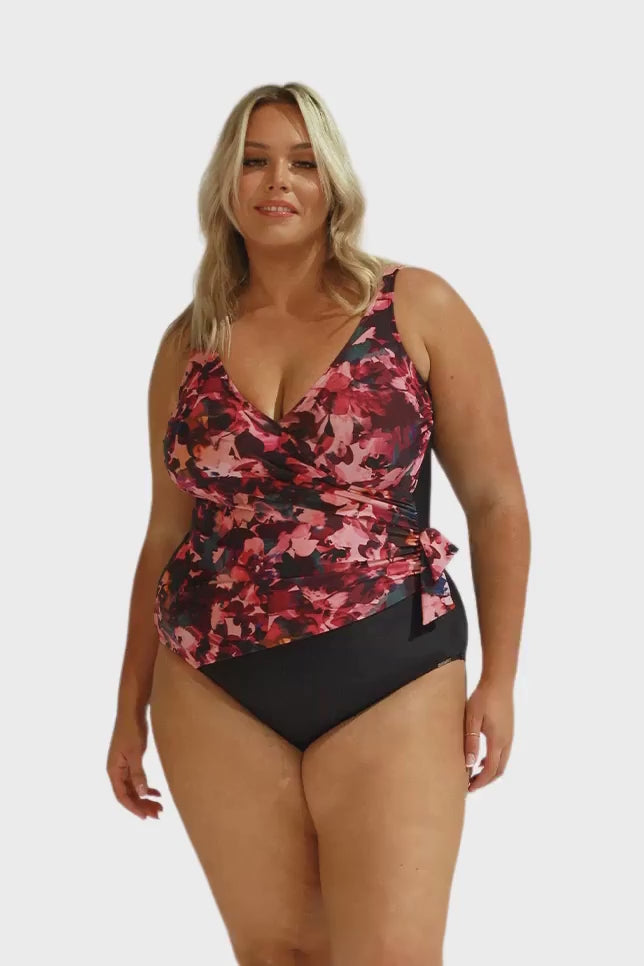 Model wearing pink, plum and black floral crossover one piece swimsuit