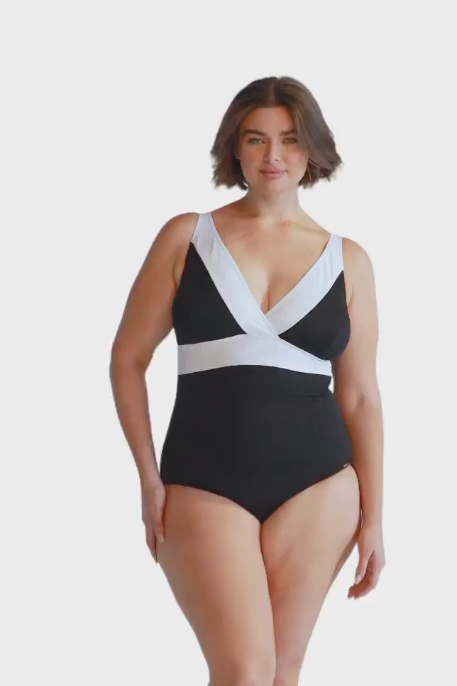 Brunette model wears black and white low v neck one piece swimsuit