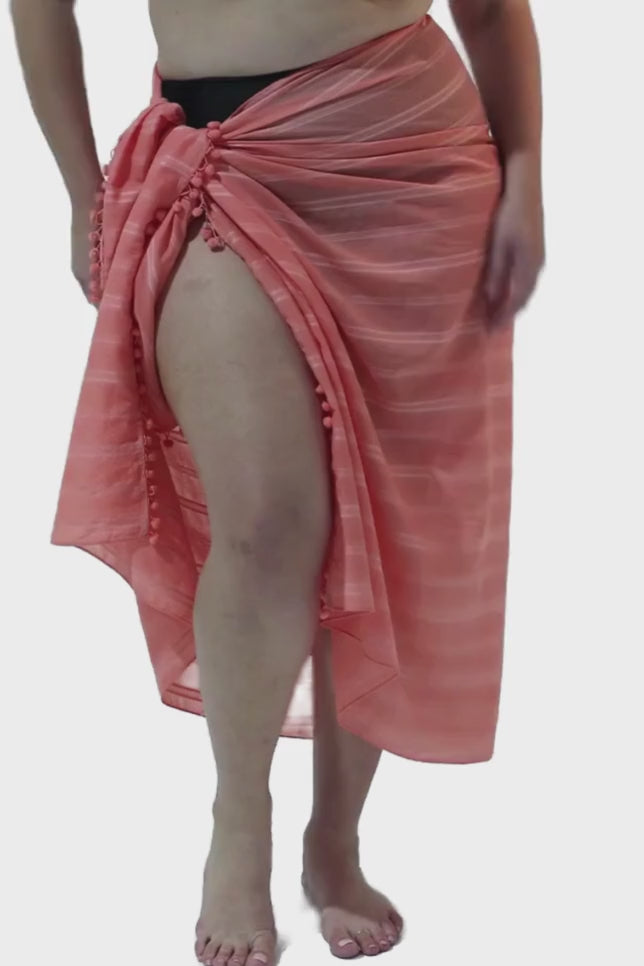Model wearing coral coloured sarong with pompom detail
