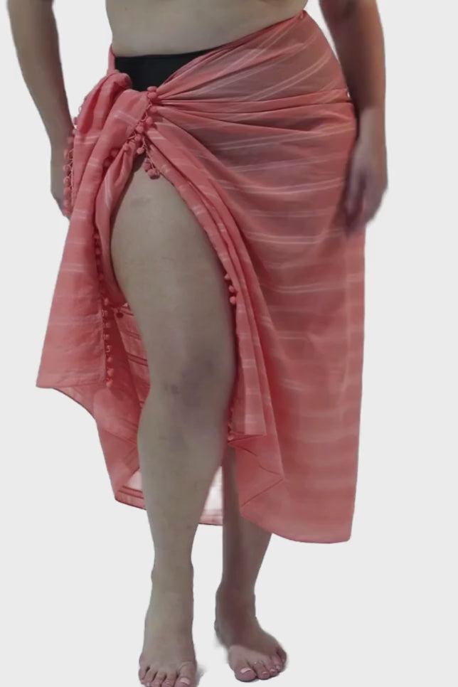 Model wearing coral coloured sarong with pompom detail