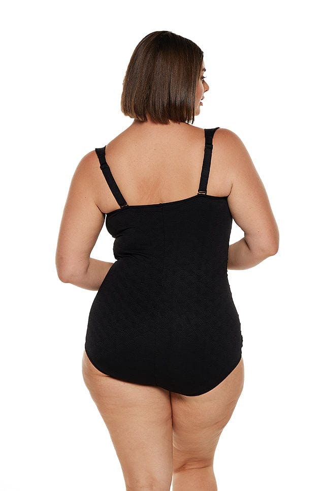 Brunette plus size model wears black textured boyleg one piece swimsuit