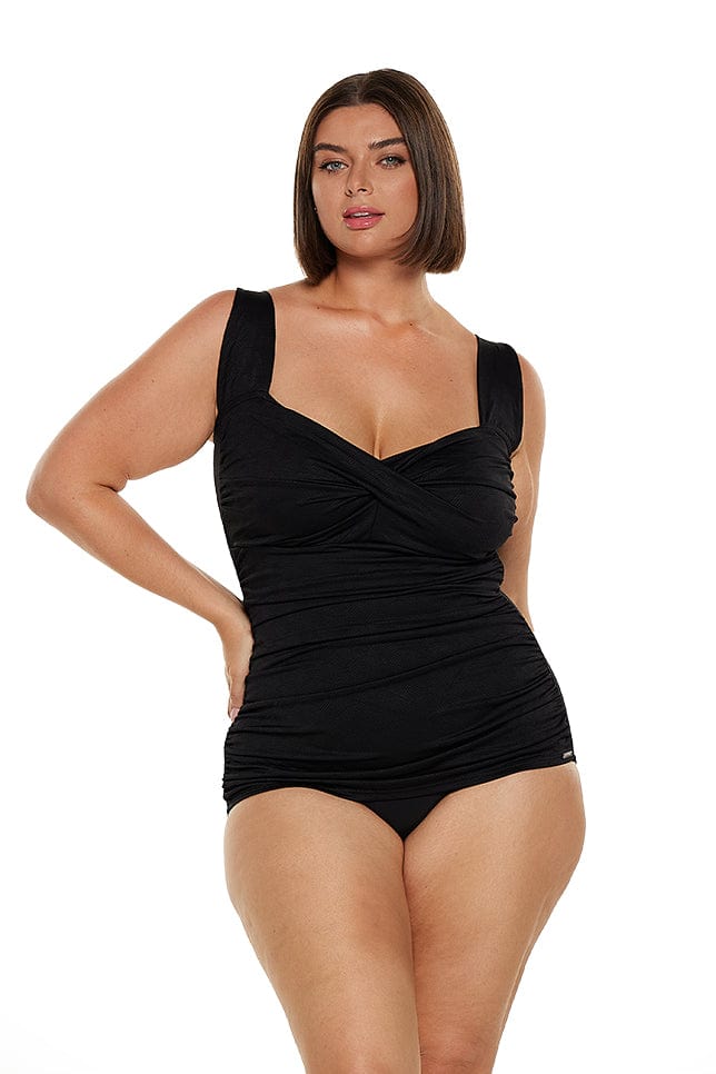 Brunette model wears black textured wide strap one piece with flattering stomach ruching and skirted pant