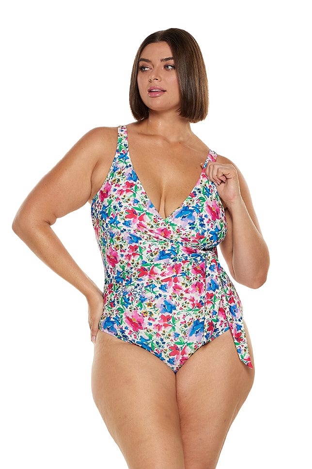 Brunette model wears low neck wrap one piece swimsuit in pink and blue floral print