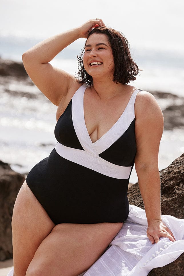Brunette women wears black and white v neck one piece swimsuit with textured fabric