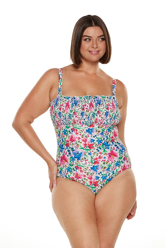 Brunette women wears shirred bandeau one piece swimsuit in bright floral print
