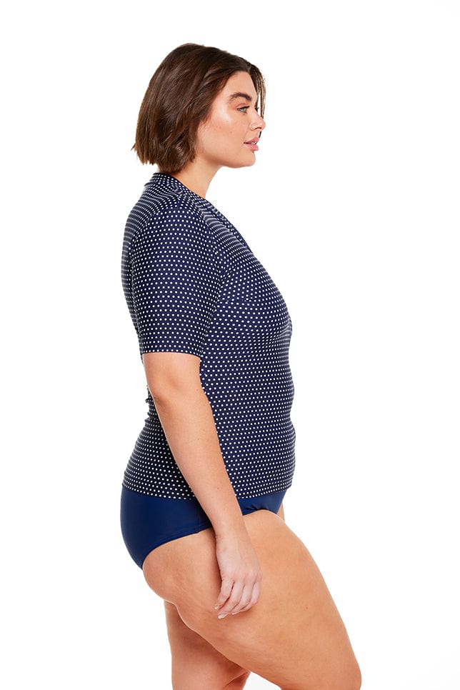 Brunette model wears navy and white dots short sleeve rash vest