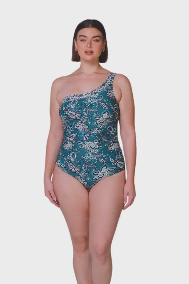 brunette model wearing one shoulder one piece swimsuit in floral green print