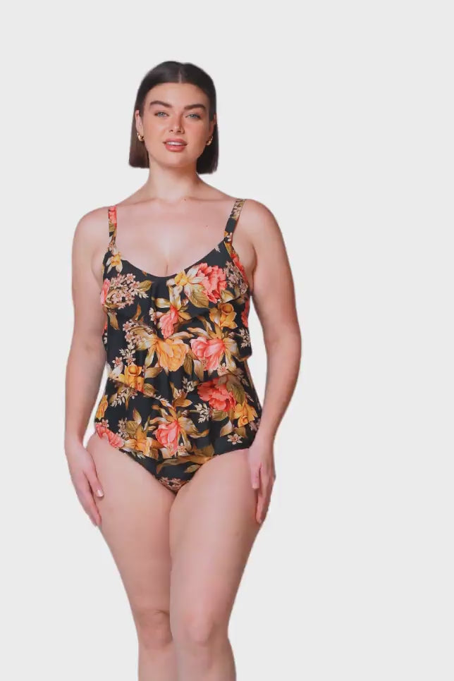 brunette australian women wearing a one piece in a  black orange and pink floral print with 3 front ruffles 