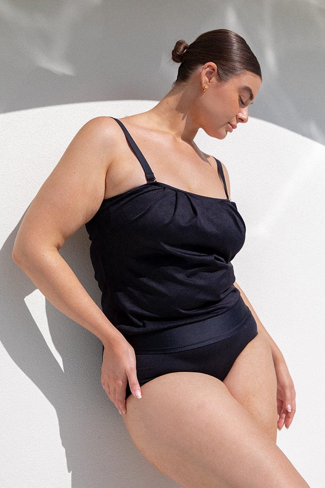 Brunette model wears flattering strapless bandeau tankini top with textured black fabric
