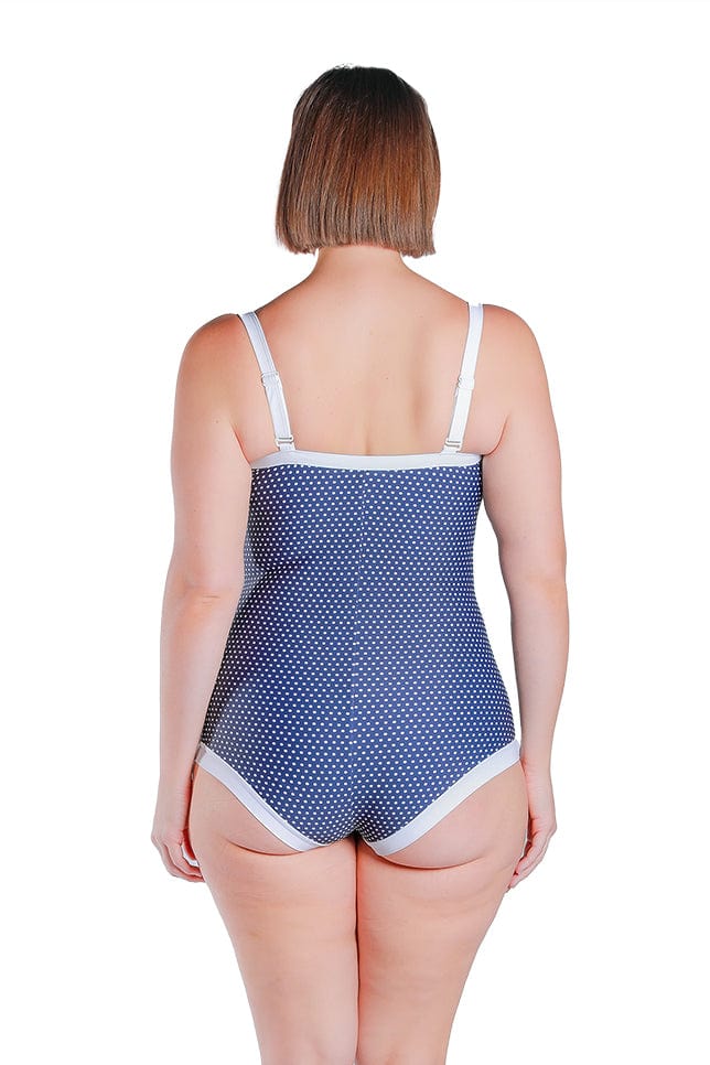 dark haired model wears retro navy and white dot swimsuit with boyleg for extra leg coverage