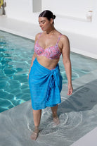 brunette women wearing blue cotton sarong with a pink bikini top at the pool